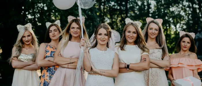 Egy menyasszony sok lufival a kezében és két oldalán egy csapat koszorúslánnyal, esküvői és elegáns ruhákban.